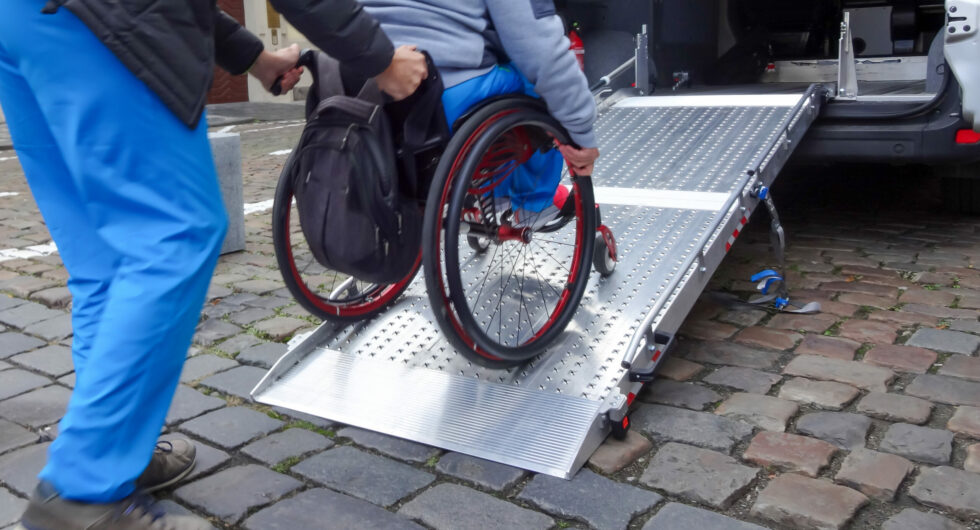 Assistant helping disabled person on wheelchair with transport using accessible van ramp